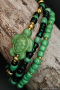 Green and black beaded bracelets with a turtle charm on a wooden surface.