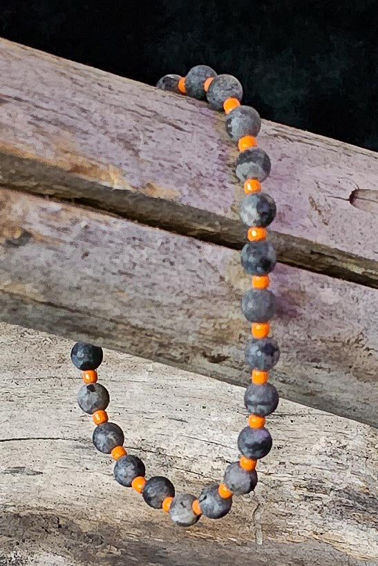 Necklace with gray and orange beads on a wooden surface