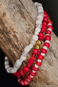 Three beaded bracelets in red, white, and gold on a wooden surface