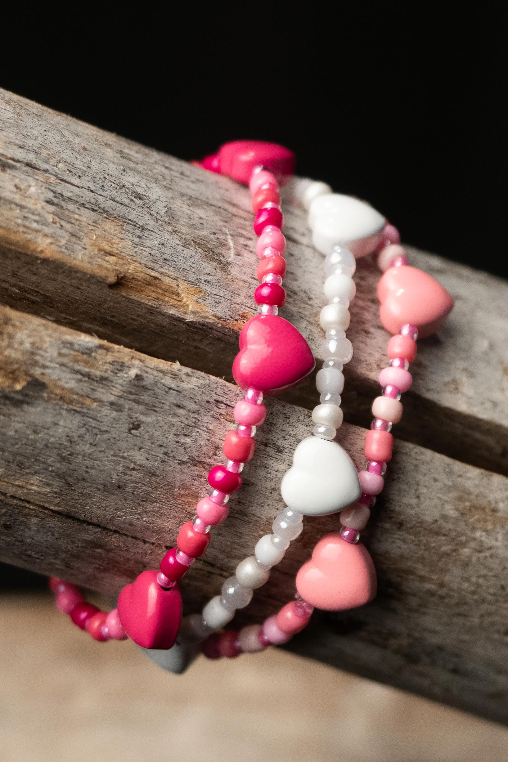 Three heart-shaped beaded bracelets on a wooden surface with a dark background