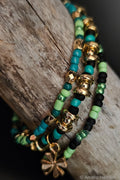 Stack of green and black beaded bracelets with gold charms and a clover charm on a wooden surface