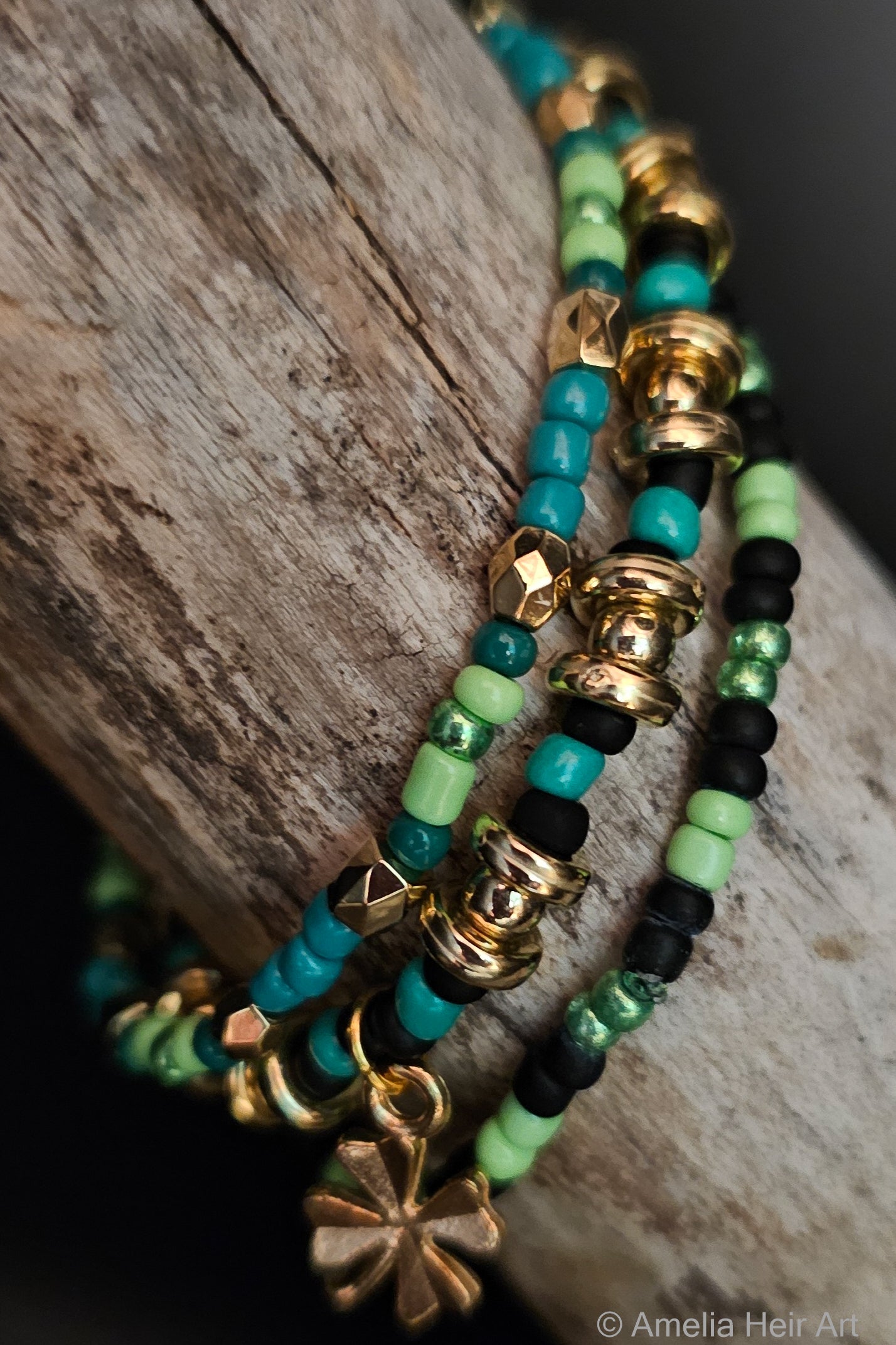 Stack of green and black beaded bracelets with gold charms and a clover charm on a wooden surface