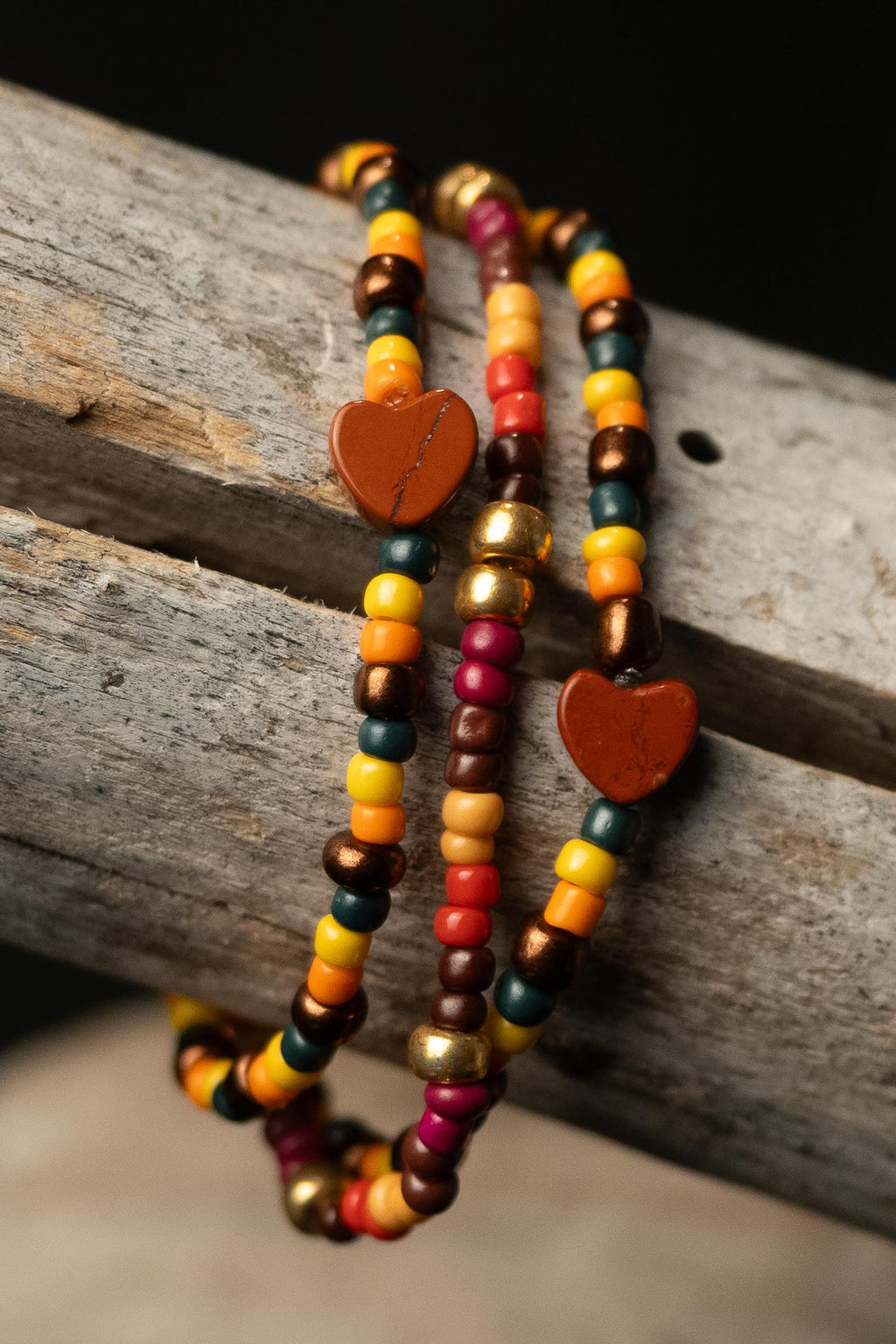 Suki handcrafted yellow red orange green gold and brown autumn beaded bracelet set with orange heart beads on a wooden surface — Amelia Heir Art