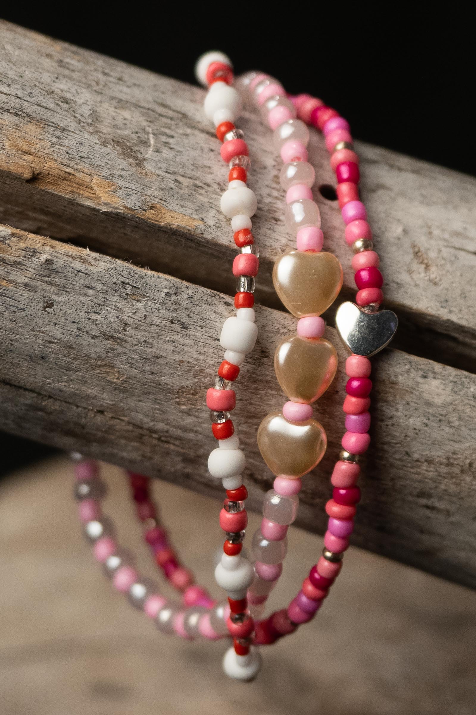 Three beaded bracelets with heart-shaped beads on a wooden surface