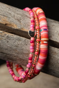 Stack of pink colorful beaded bracelets with a heart accent on a wooden surface