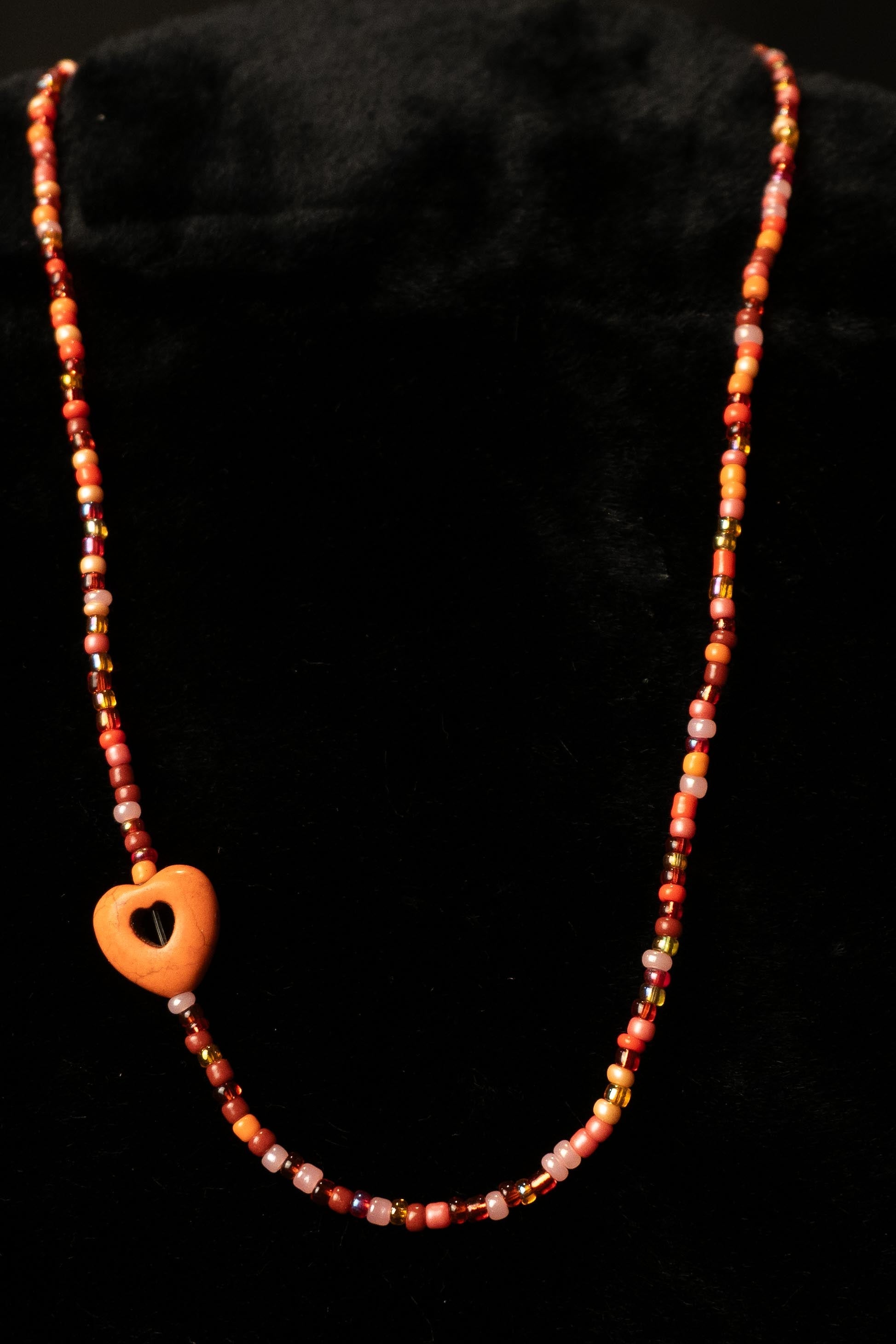 Necklace with orange beads and a heart-shaped pendant on a black background