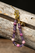 Beaded chain with pink and purple beads and a gold heart charm on a wooden surface