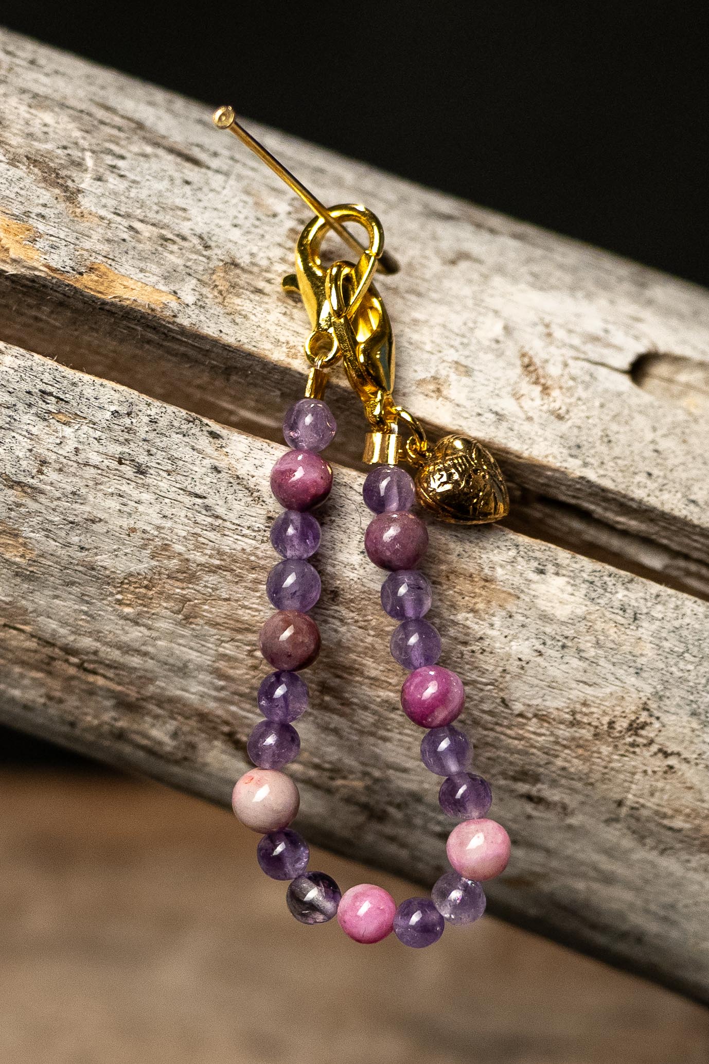Beaded chain with pink and purple beads and a gold heart charm on a wooden surface