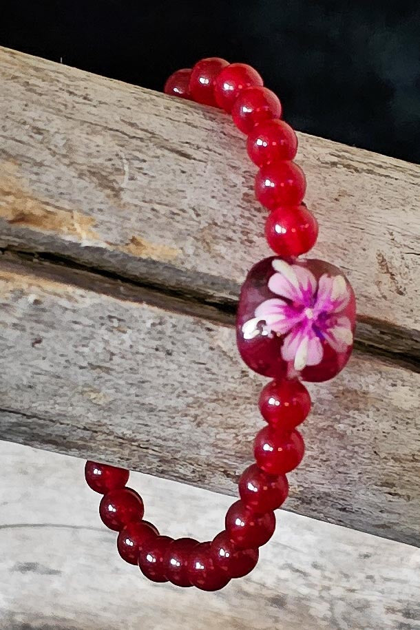 Red beaded bracelet with a floral glass bead on a wooden surface