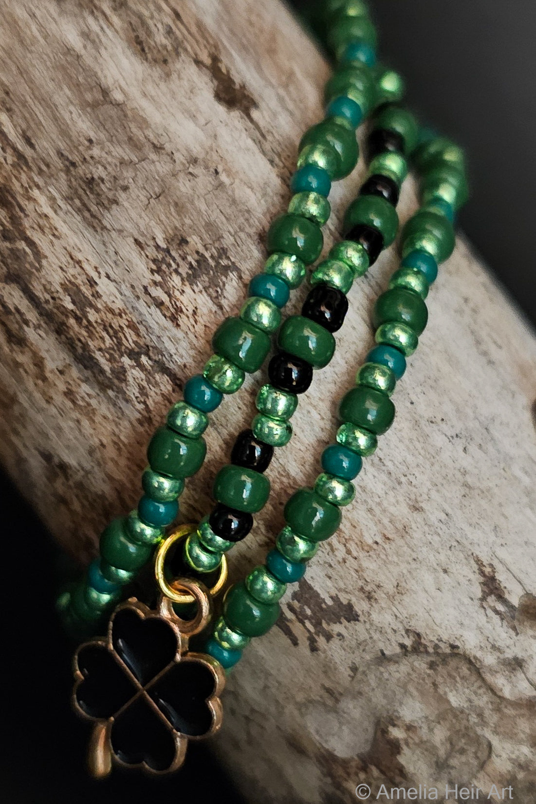 Green beaded bracelet with a gold and black clover charm on a wooden surface