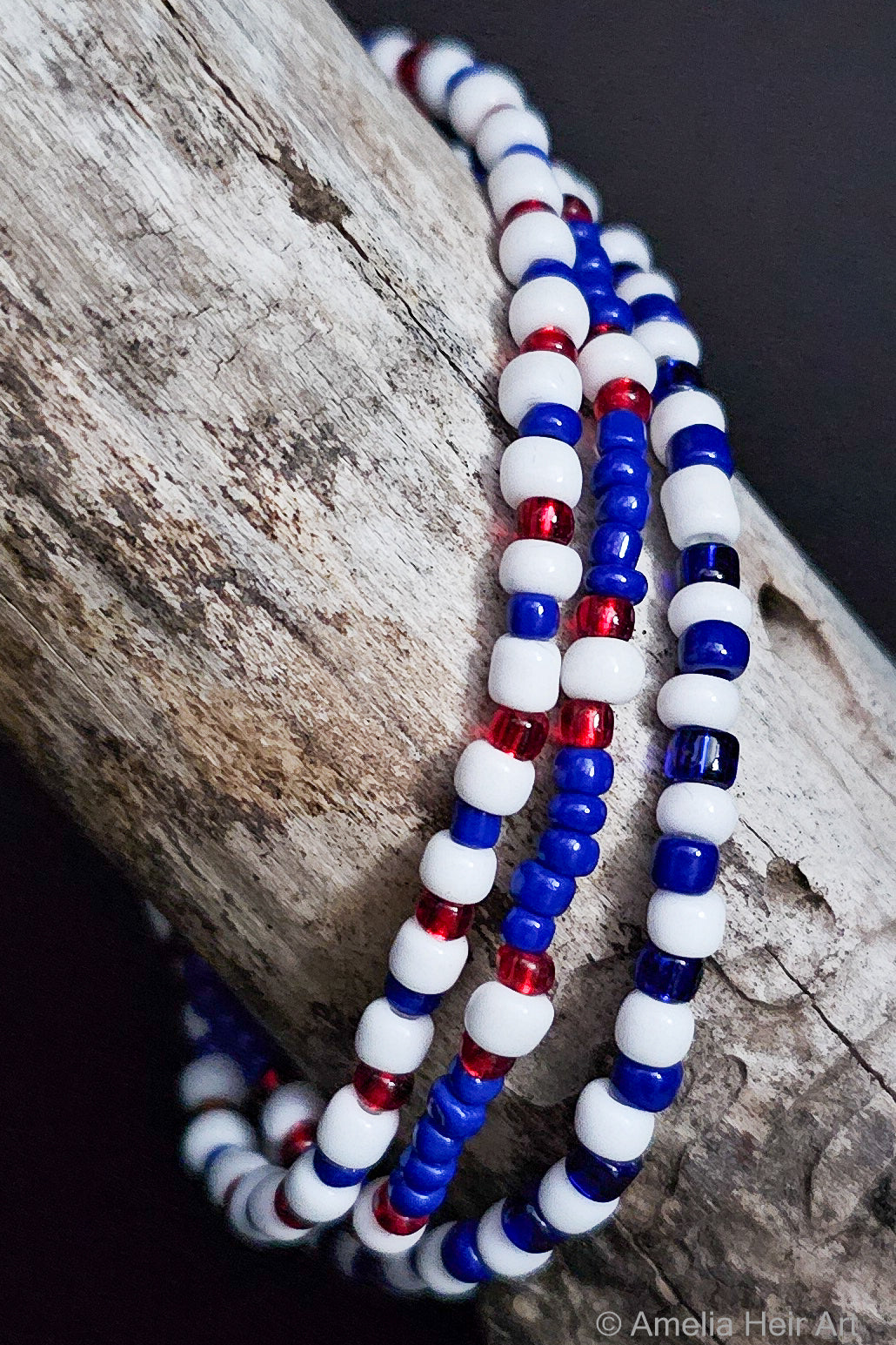 Three beaded bracelets in red, white, and blue on a wooden surface.