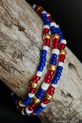 Three beaded bracelets in red, white, and blue beads on a wooden surface.