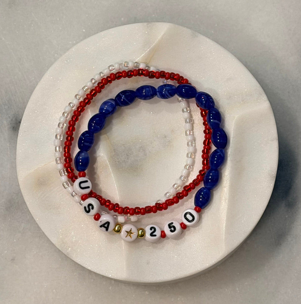 Americana Collection, 250 Anniversary, three red, white, and blue beaded bracelets with 'USA' and 250 numbers on a marble circle, Amelia Heir Art