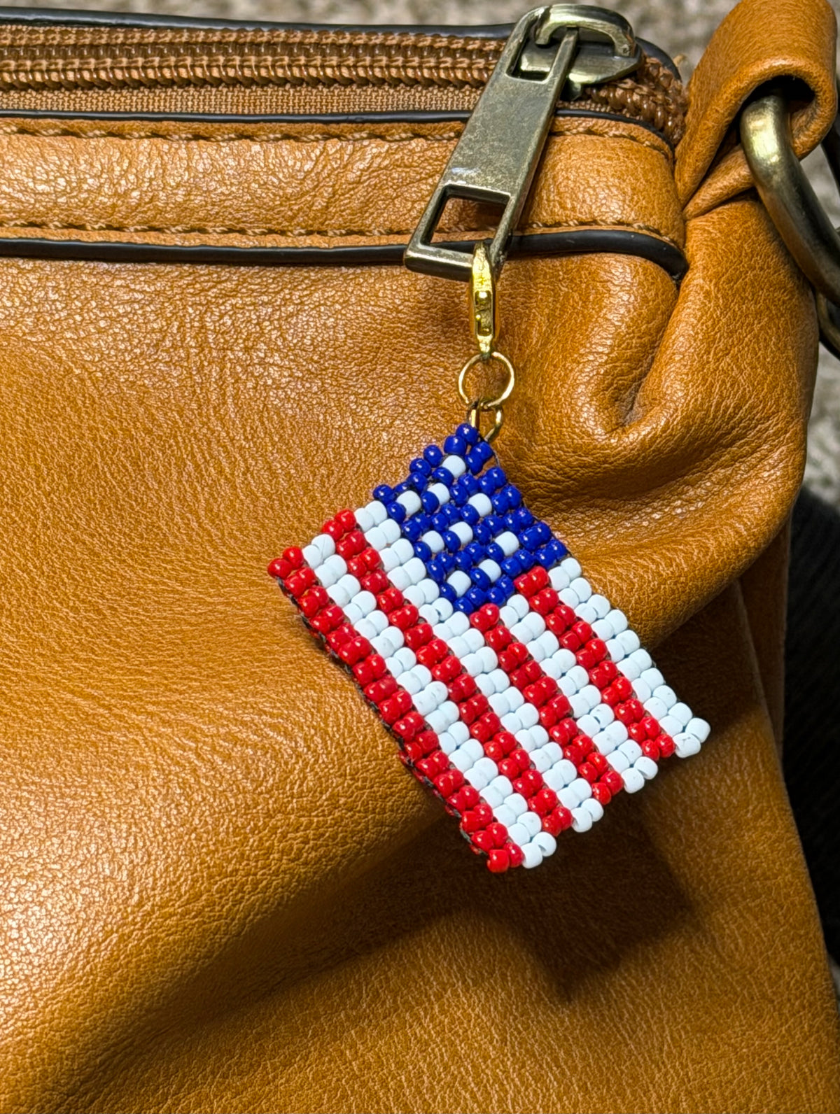 Close-up of Pledge handmade zipper pull by Amelia Heir Art, featuring a red, white, and blue beaded American flag attached to a brown purse zipper.