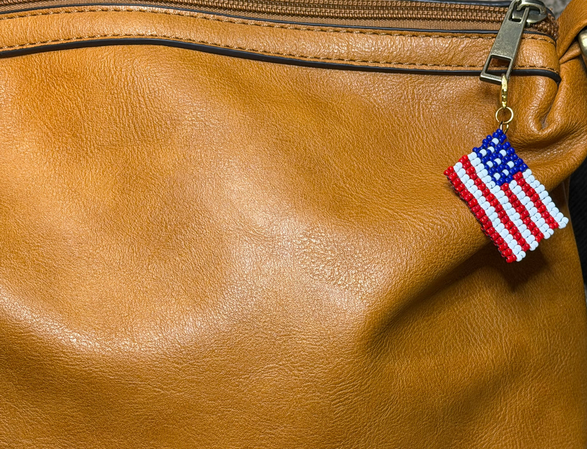 Pledge handmade zipper pull by Amelia Heir Art, featuring a red, white, and blue beaded American flag shown on a brown purse for scale.
