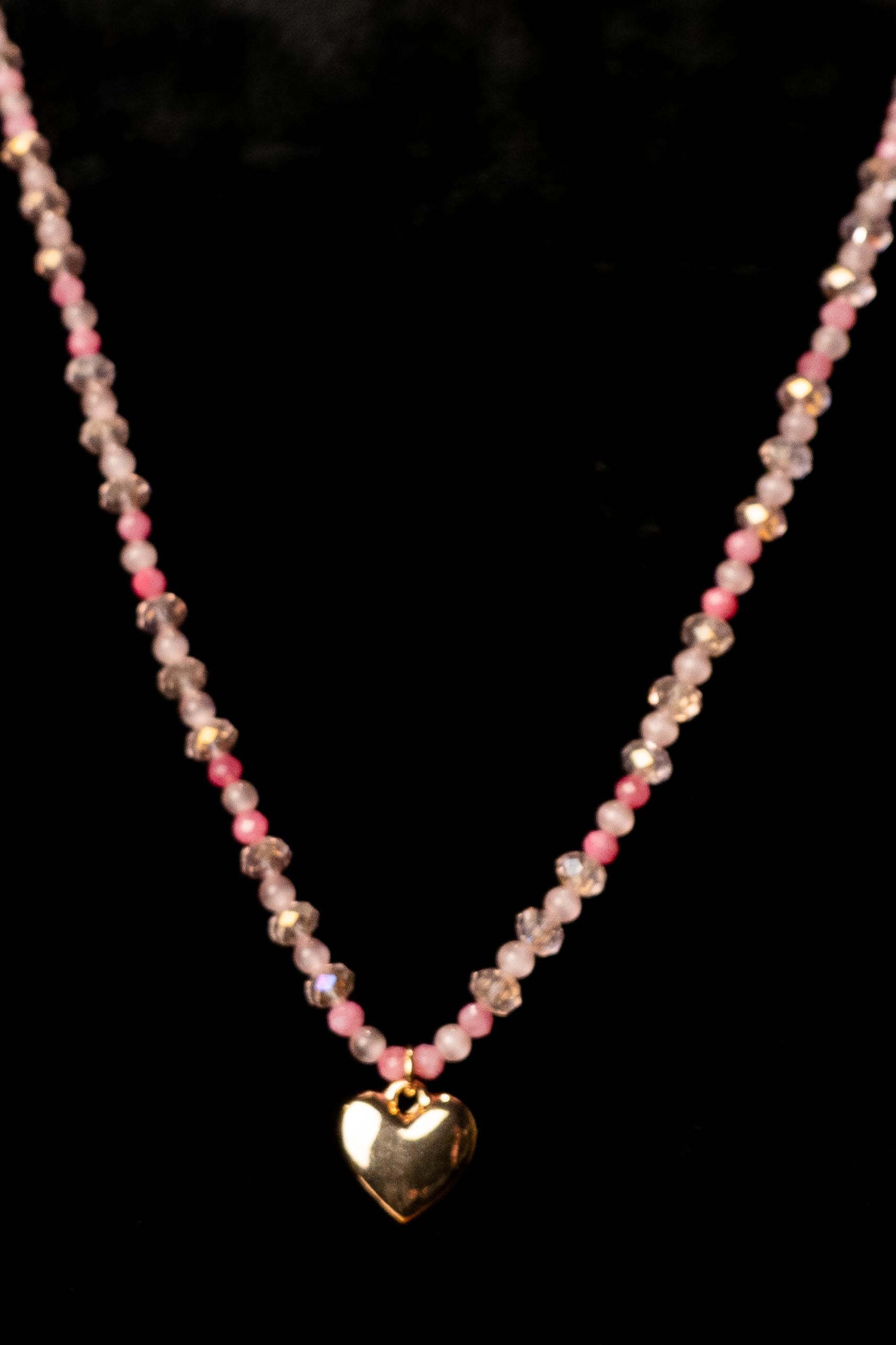 Necklace with pink beads and a gold heart pendant on a black background