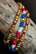 Three beaded bracelets with gold, red, white, and blue beads on a wooden surface.