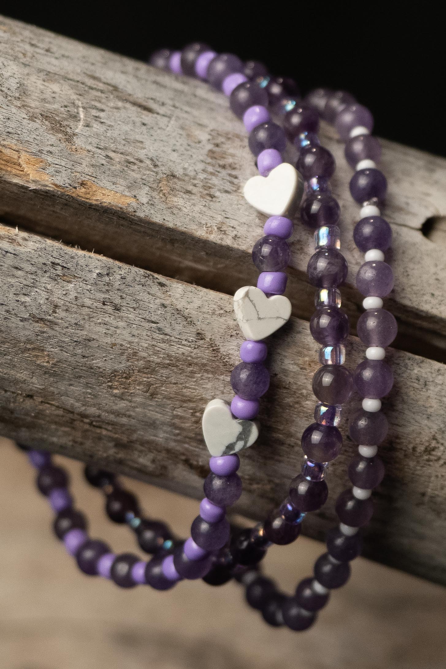 Purple beaded bracelets with white heart charms on a wooden surface