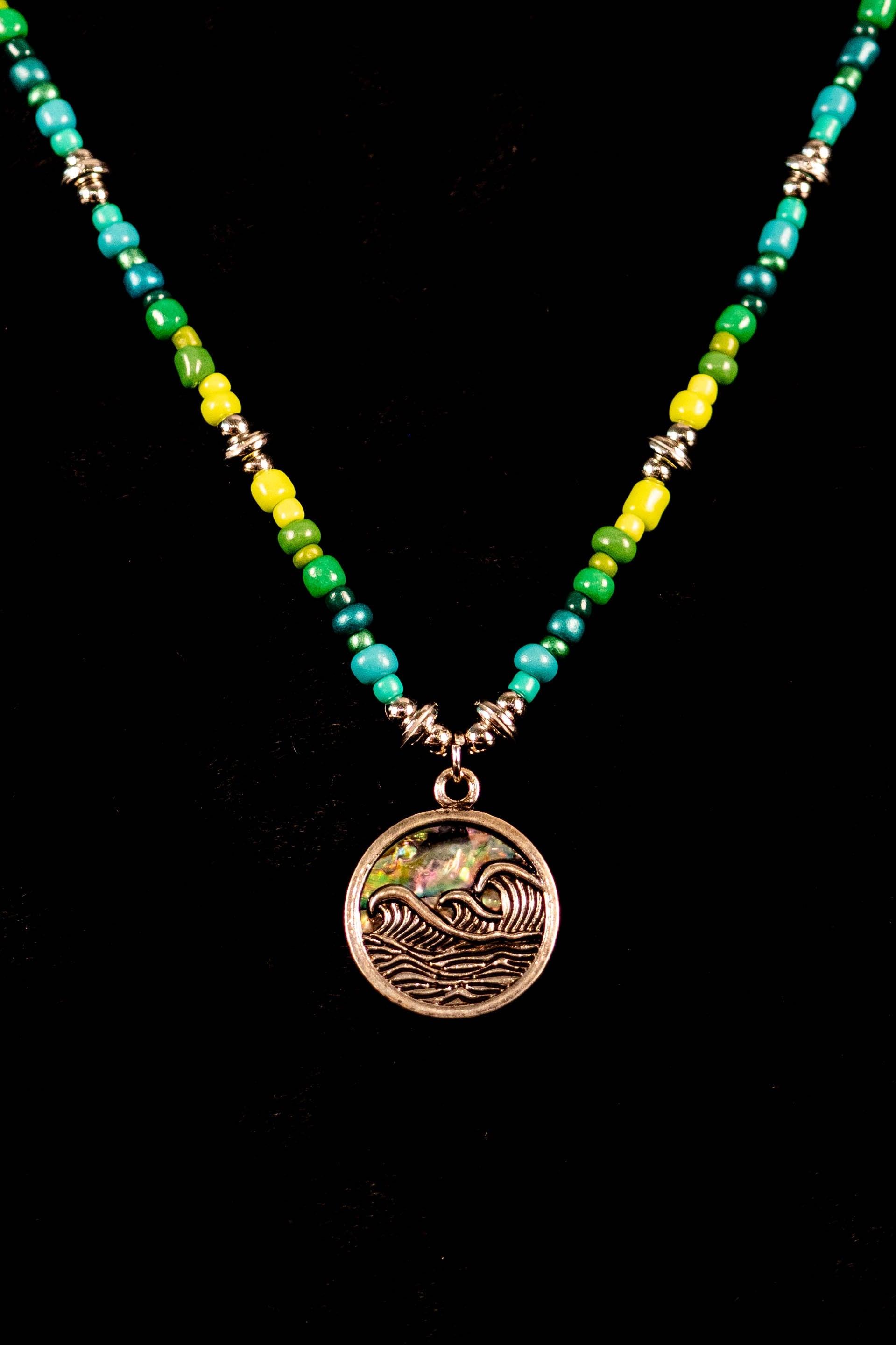Necklace with green and yellow beads and a silver pendant with a wave on a black background.