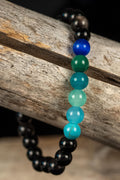 Beaded bracelet with black, blue, and green beads on a wooden surface
