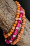 Orange and pink beaded bracelets on a wooden surface.