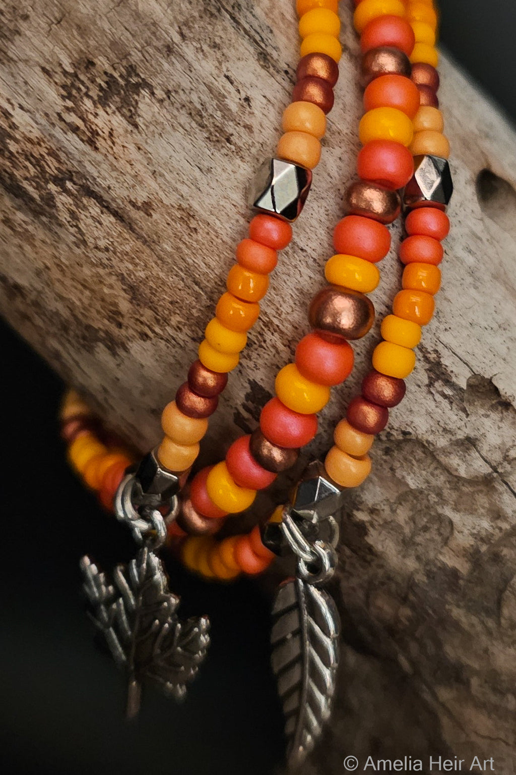 Wind handcrafted yellow, pink, orange & copper beaded bracelet set with leaf and feather charms on a wooden surface — Amelia Heir Art