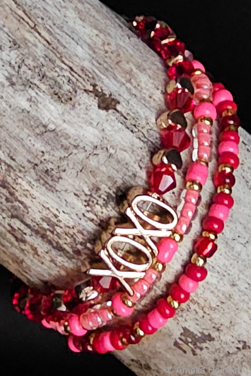 Stack of pink beaded bracelets with 'XOXO' design on a wooden surface